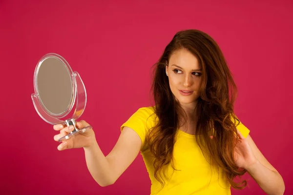 Atractiva joven mujer se mira en el espejo sobre vibrante rosa — Foto de Stock