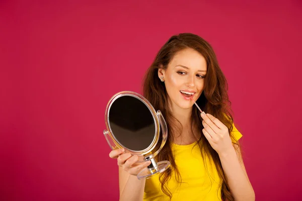 Atrakcyjna, młoda kobieta, stosując błyszczyk, patrząc w lustro — Zdjęcie stockowe
