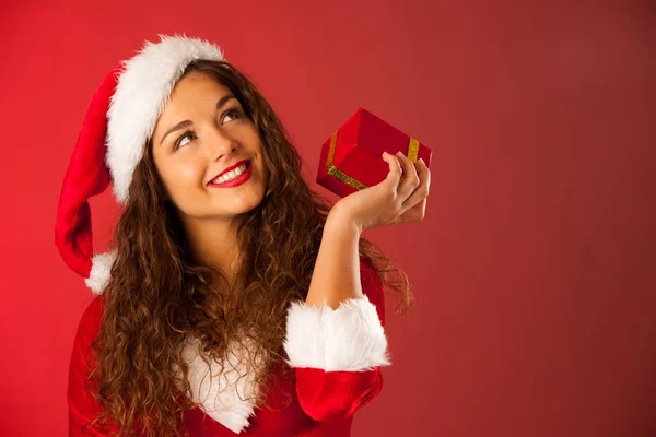 Bela jovem mulher no Santa vestido detém um presente sobre vermelho ba — Fotografia de Stock