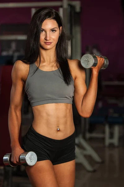 Hermosa mujer deportiva ejercita sus brazos en gimnasio de fitness — Foto de Stock