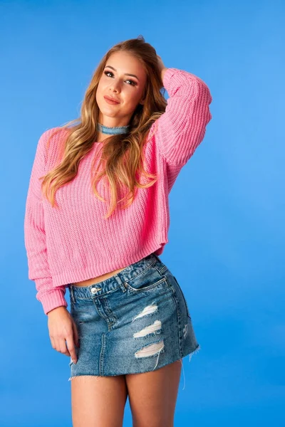 Piękna młoda kobieta w różowy sweter i dżinsy Spódniczka na niebieskim tle — Zdjęcie stockowe