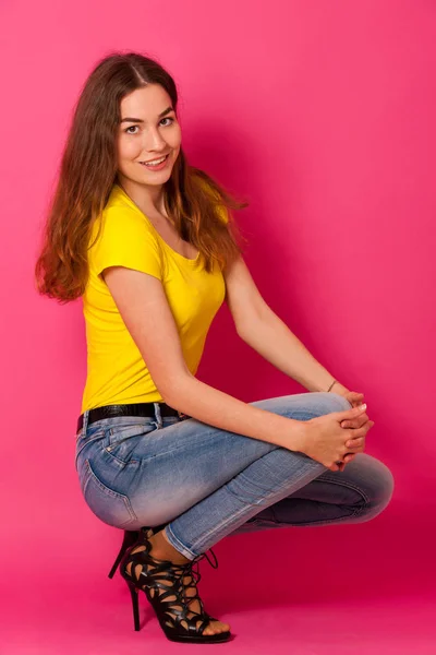 Atractiva joven en jeans y camiseta amarilla sobre bac rosa — Foto de Stock