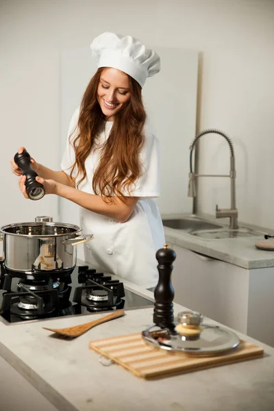 Beautiful young woman in white chef uniform cooking in the kitch — Stock Photo, Image