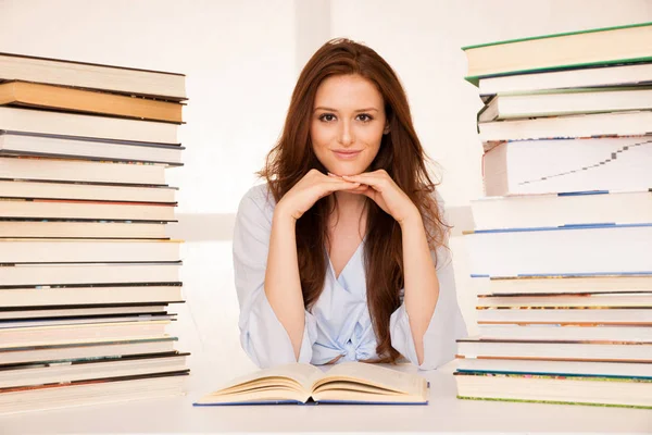Attractive young woman studies wtih hugr book piles on her desk — Stock Photo, Image