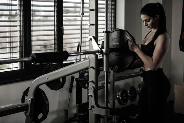 Mujer añadiendo peso en un bar mientras se ejercita en el gimnasio de fitness — Foto de Stock