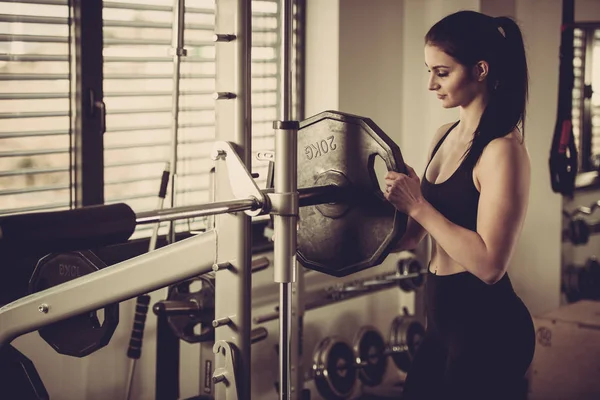 Mujer añadiendo peso en un bar mientras se ejercita en el gimnasio de fitness — Foto de Stock