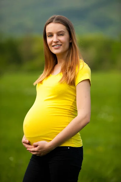 Schwangere Frau im gelben T-Shirt auf einer grünen Wiese im Frühling — Stockfoto