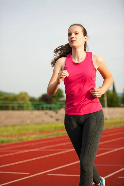 一个美丽的年轻女子赛跑选手在夏初的下午在跑道上跑步 — 图库照片
