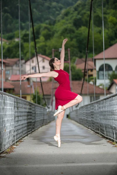年轻美丽的芭蕾舞演员穿着红衣服在桥上跳舞 — 图库照片