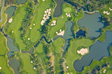Golf sahasının havadan görünüşü ve kum tuzakları, ağaçlar ve golfçülerle dolu yeşil. 