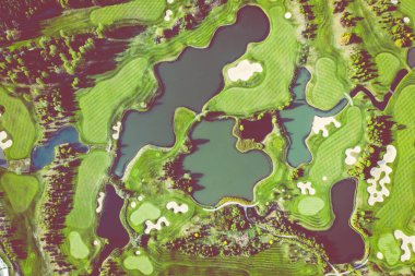 Golf sahasının havadan görünüşü ve kum tuzakları, ağaçlar ve golfçülerle dolu yeşil. 
