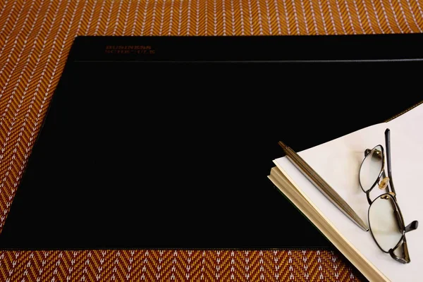 Blocco note penna occhiali e pad scrivania in vinile nero su tappetino marrone — Foto Stock
