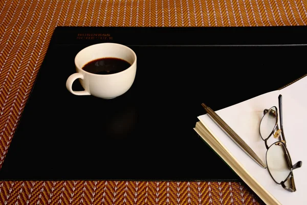 Taza de café negro, cuaderno, bolígrafo, gafas y escritorio de vinilo negro p —  Fotos de Stock