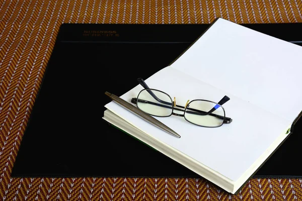 Notebook pen eyeglass and Black vinyl desk pad on brown mat — ストック写真