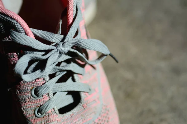 Modern pink sport shoes with gray shoelace on natural background.