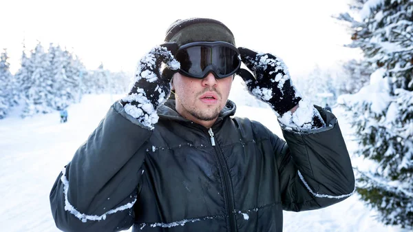 Snowboarder de pé em uma pista de esqui no inverno e mantém suas mãos uma máscara de esqui — Fotografia de Stock