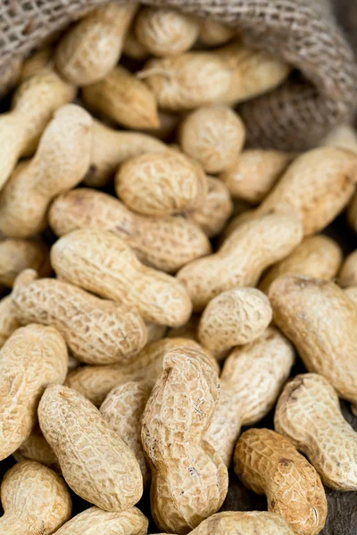 Cacahuetes en una bolsa de arpillera miniatura en superficie de madera — Foto de Stock