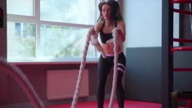 Genç bir kız spor salonunda çapraz formda idman yaparken halat egzersizi yapıyor.
