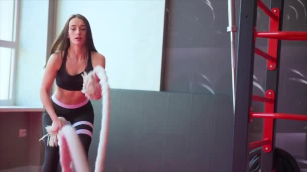 Chica adulta joven practicando ejercicio de cuerda de batalla durante un entrenamiento crossfit en el gimnasio — Vídeos de Stock