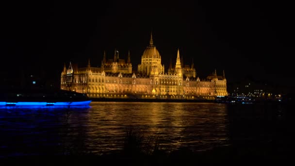 布达佩斯国民议会在夜间开灯。 多瑙河的前景，4k处的帆船 — 图库视频影像