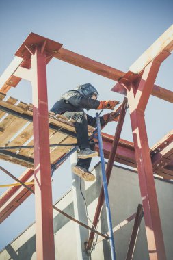 Maskeli kaynakçı büyük bir inşaat alanında metal kaynaklıyor.