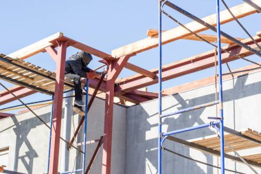 Maskeli kaynakçı büyük bir inşaat alanında metal kaynaklıyor.