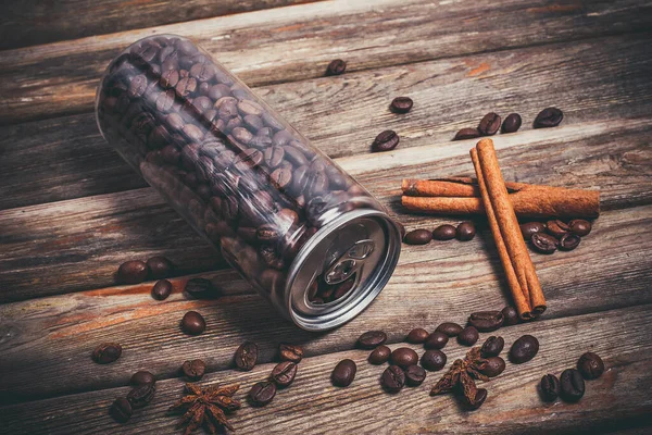 Coffee grains in a plastic jar and grains lie nearby on a wooden table