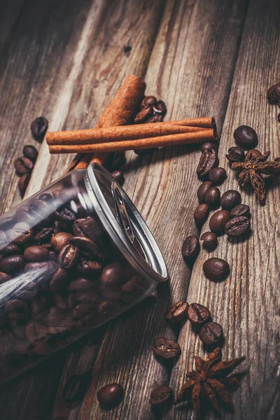 Coffee grains in a plastic jar and grains lie nearby on a wooden table