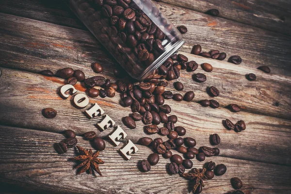 Coffee grains in a plastic jar and grains lie nearby on a wooden table