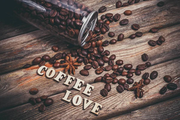 Coffee grains in a plastic jar and grains lie nearby on a wooden table