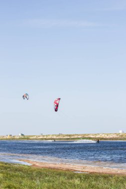 Atlet, sıcak yaz mevsiminde atlayışlar ve hilelerle denizde uçurtma sürüyor..