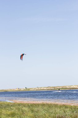 Atlet, sıcak yaz mevsiminde atlayışlar ve hilelerle denizde uçurtma sürüyor..