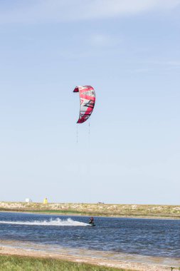 Atlet, sıcak yaz mevsiminde atlayışlar ve hilelerle denizde uçurtma sürüyor..