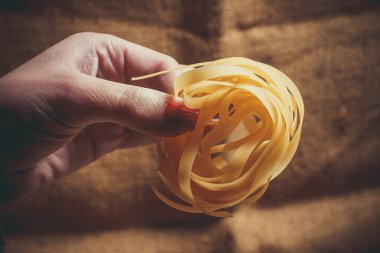 Ahşap arka planda makarna pişirmek için bir kızın ellerinde çiğ makarna.