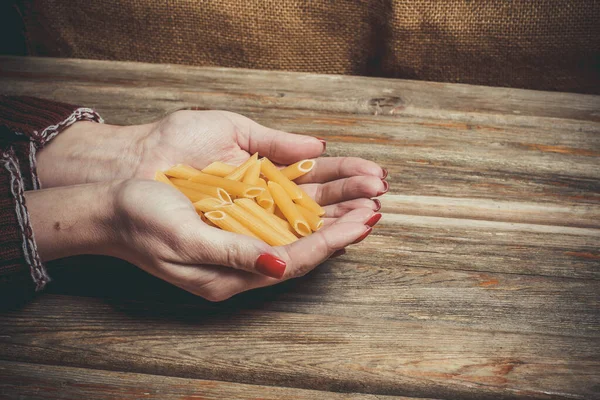 Raw pasta in the hands of a girl for cooking pasta on a wooden background