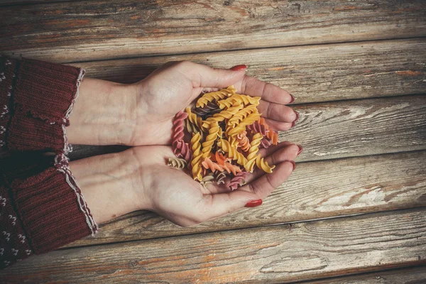 Raw pasta in the hands of a girl for cooking pasta on a wooden background