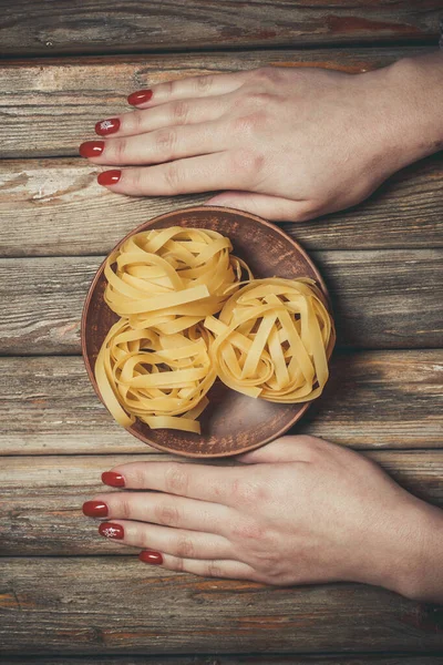 Raw pasta in the hands of a girl for cooking pasta on a wooden background