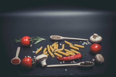 Sebzeli çiğ makarna ve siyah bir yüzeyde baharatlar.