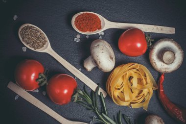 Sebzeli çiğ makarna ve siyah bir yüzeyde baharatlar.