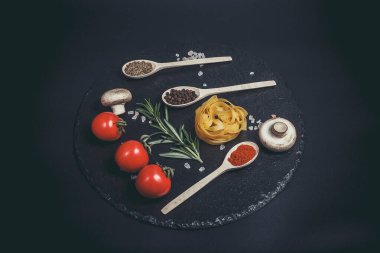 Sebzeli çiğ makarna ve siyah bir yüzeyde baharatlar.