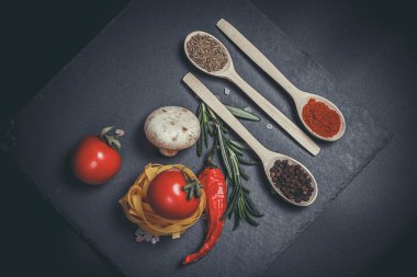 Sebzeli çiğ makarna ve siyah bir yüzeyde baharatlar.