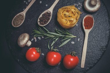 Sebzeli çiğ makarna ve siyah bir yüzeyde baharatlar.