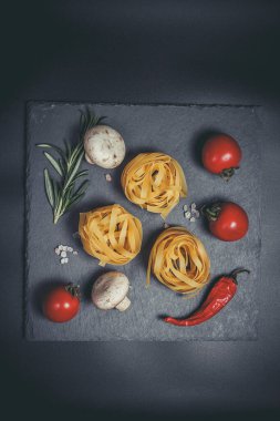 Sebzeli çiğ makarna ve siyah bir yüzeyde baharatlar.