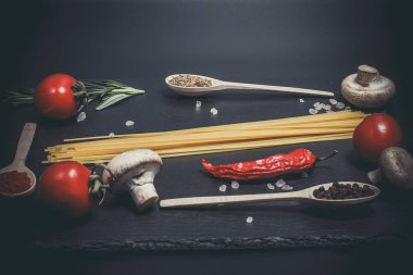 Sebzeli çiğ makarna ve siyah bir yüzeyde baharatlar.