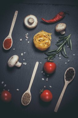 Sebzeli çiğ makarna ve siyah bir yüzeyde baharatlar.