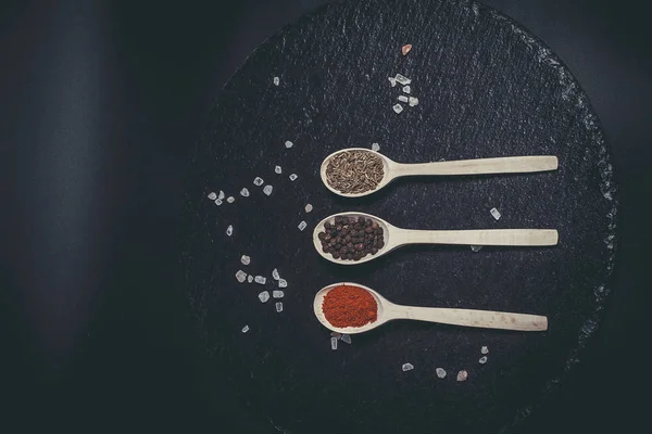 Fragrant spices in spoons on a black surface