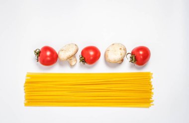 Çiğ makarna, taze sebzeler, domatesler ve mantarlar kapalı beyaz bir tabakta.