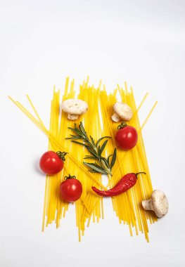 Çiğ makarna, taze sebzeler, domatesler ve mantarlar kapalı beyaz bir tabakta.