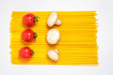 Çiğ makarna, taze sebzeler, domatesler ve mantarlar kapalı beyaz bir tabakta.
