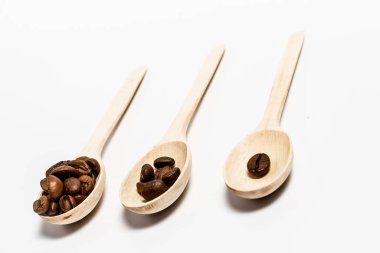Beyaz arka planda hafif ahşap kaşıklarda mis kokulu kahve taneleri